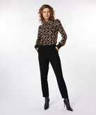 Woman wearing a patterned blouse, black pants, and black boots on a white background