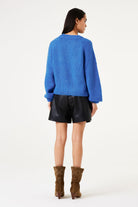 Woman wearing a blue sweater, black leather shorts, and brown boots on a white background